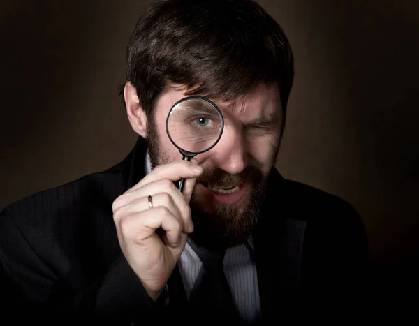 Portrait de beau jeune homme d'affaires regardant à travers la loupe sur un fond brun — Photo