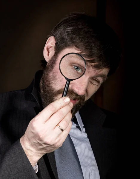 Portrait de beau jeune homme d'affaires regardant à travers la loupe sur un fond brun — Photo