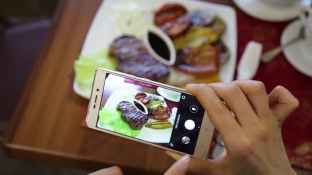 レストランでトレンディな女性は社会的ネットワークの携帯電話のカメラで料理の写真を作る — ストック動画