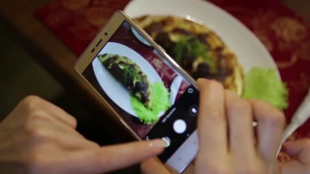 レストランでトレンディな女性は社会的ネットワークの携帯電話のカメラで料理の写真を作る — ストック動画