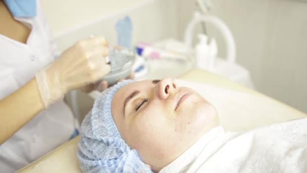 Cosmetologist aplicando máscara facial para mulher bonita no salão de beleza — Vídeo de Stock