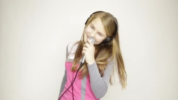 Young girl listening music on headphones holding microphone, singing and funy dancing — Stock Video