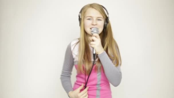 Young girl listening music on headphones holding microphone, singing and funy dancing — Stock Video