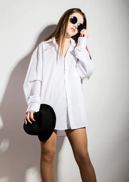Naked girl in a mans white shirt, sunglasses and black hat — Stock Photo, Image