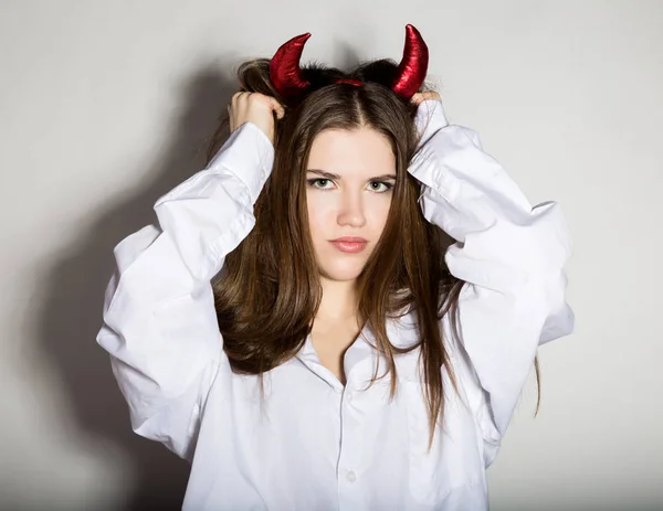 Joven chica en un mans blanco camisa con cuernos rojos parece bonito diablo — Foto de Stock
