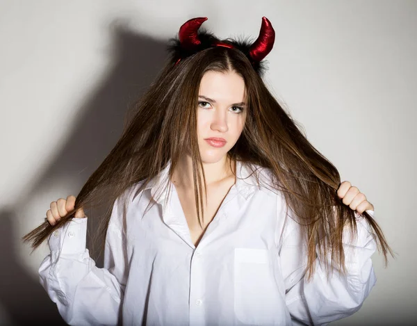 Mladá dívka v mans bílou košili s červenými rohy vypadá docela ďábel — Stock fotografie