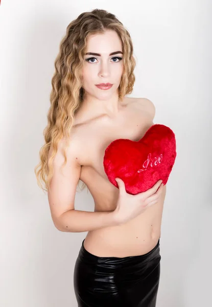 Jeune et belle fille bouclée avec corps nu, tenant un oreiller coeur rouge — Photo