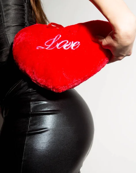 Giovane bella ragazza in un corsetto di pelle con allacciatura e gonna, tenendo cuscino cuore rosso — Foto Stock