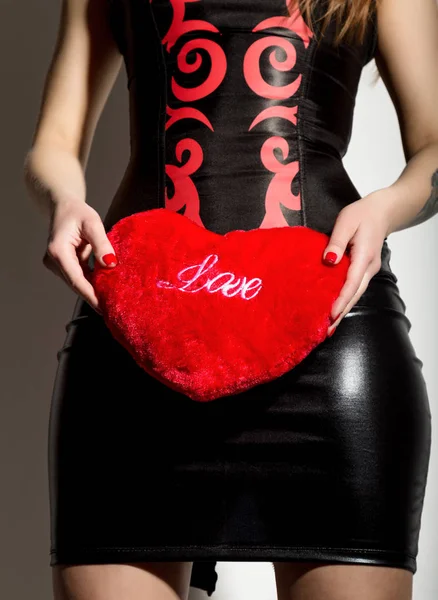 Mladá a krásná dívka v Kožený korzet se šněrováním a sukni, držící červené srdce polštář — Stock fotografie