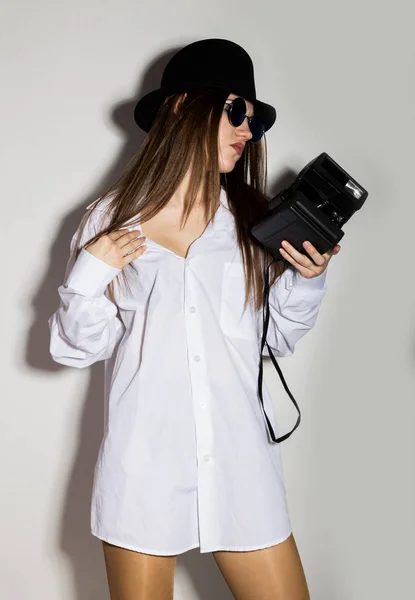 Chica desnuda en una camisa blanca mans, gafas de sol y sombrero negro, celebración de la cámara — Foto de Stock