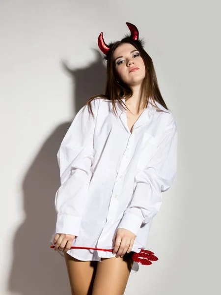 Jovem menina em um homem camisa branca com chifres vermelhos segurando tridente e parece muito Diabo — Fotografia de Stock