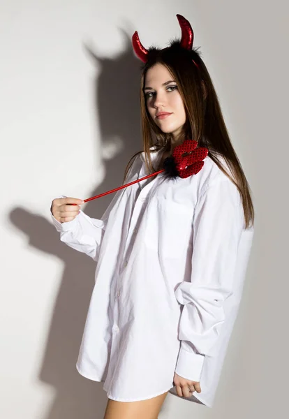 Jovem menina em um homem camisa branca com chifres vermelhos segurando tridente e parece muito Diabo — Fotografia de Stock