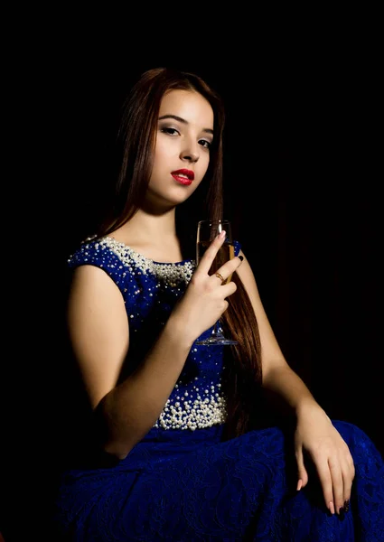 Giovane donna celebrante in un abito blu che tiene un bicchiere di champagne, sfondo scuro. giocare luce e shedow — Foto Stock