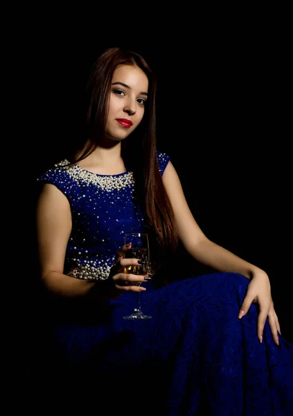 Junge feiernde Frau in blauem Kleid mit einem Glas Champagner vor dunklem Hintergrund. Licht und Schatten spielen — Stockfoto