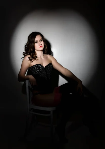Sexy chica en ropa interior de encaje y corsé, sentado en la silla posando en el estudio un fondo oscuro — Foto de Stock