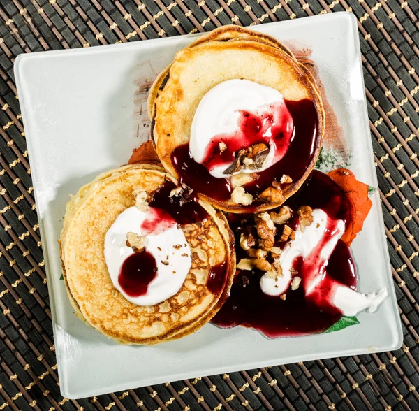 stock image Homemade sweet pancakes with fruit jam, sour cream on a white plate. Breakfast with stack topped blueberry jam and walnuts.