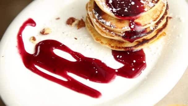 Hemmagjord söta pannkakor med frukt sylt, gräddfil på en vit platta. Frukost med stack toppad blåbär sylt och valnötter. — Stockvideo