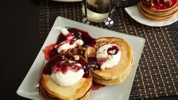 Hausgemachte süße Pfannkuchen mit Fruchtmarmelade, saure Sahne auf einem weißen Teller. Frühstück mit Blaubeermarmelade und Walnüssen. — Stockvideo