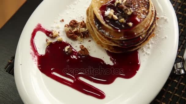 Zelfgemaakte zoete pannenkoeken met fruit jam en zure room op een witte plaat. Ontbijt met stapel bijgevuld bosbessen jam en walnoten. — Stockvideo