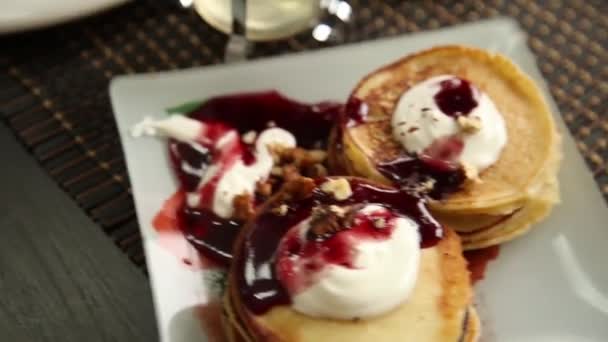 Hemmagjord söta pannkakor med frukt sylt, gräddfil på en vit platta. Frukost med stack toppad blåbär sylt och valnötter. — Stockvideo