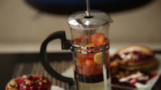 Ontbijt met stapel bijgevuld bosbessen jam, walnoten en theepot met vruchten thee. Zelfgemaakte zoete pannenkoeken met jam, zure room op een witte plaat. — Stockvideo