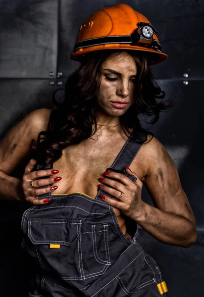 close-up portrait sexy female miner worker in coveralls over his naked body, helmet on the head with a flashlight