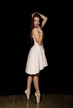 Kusursuz bir beden ile genç balerin pointe yerinde koyu arka plan üzerinde dans ediyor