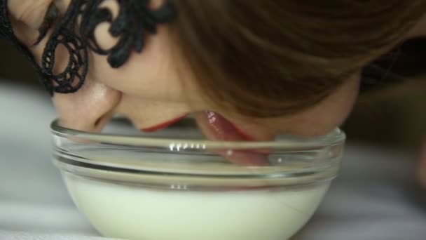 Крупный план молодой сексуальной женщины в кружевной маске, пьющей молоко, как кошка. Улыбающаяся девушка, ласкающая йогурт из стеклянных чаш — стоковое видео