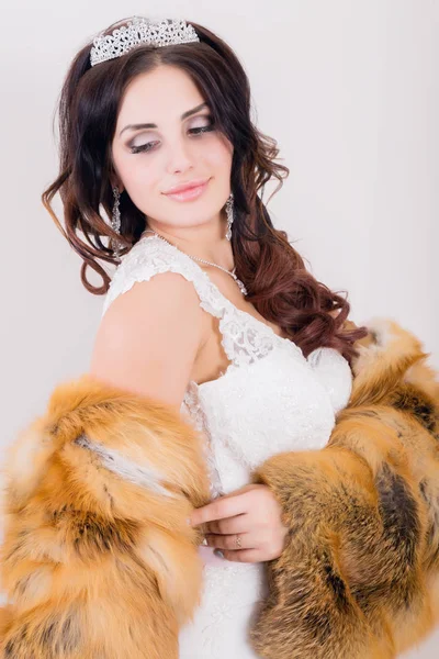 Bela noiva jovem vestindo vestido de noiva branco e casaco de pele com maquiagem profissional — Fotografia de Stock