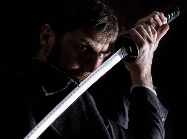 Aktern arg affärsman i en ullkappa med svärd i mörk bakgrund — Stockfoto
