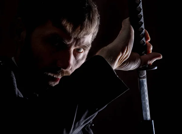 Строгий сердитый бизнесмен в шерстяном пальто с мечом на темном фоне — стоковое фото