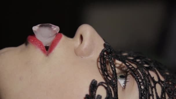 Jeune femme séduisante en masque de dentelle tenant un glaçon dans la bouche avec des lèvres claret — Video