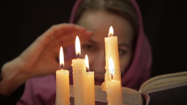 在做魔法仪式头巾的女人。几个蜡烛的特写和旧书。万圣节或宗教的概念 — 图库视频影像
