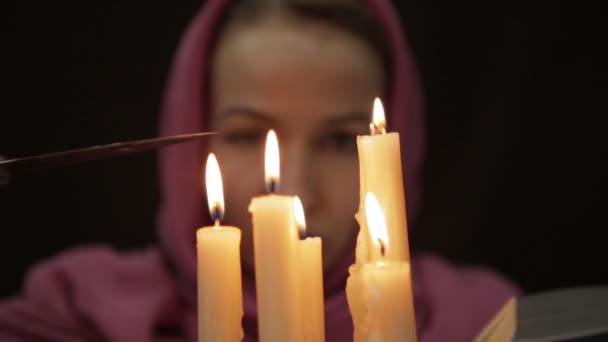 Una mujer con un pañuelo en la cabeza haciendo el ritual mágico. primer plano varias velas y libro viejo. halloween o concepto de religión — Vídeo de stock