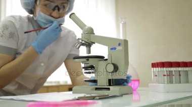 mikroskoplar ve laboratuvar koşullarında test tüpleri ile çalışan kadın tıbbi araştırmacılar inceler ve notlar alır