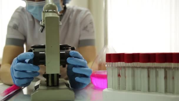 Θηλυκό ιατρικούς ερευνητές που εργάζονται με μικροσκόπια και τους σωλήνες δοκιμής σε συνθήκες εργαστηρίου, ερευνά και παίρνει σημειώσεις — Αρχείο Βίντεο