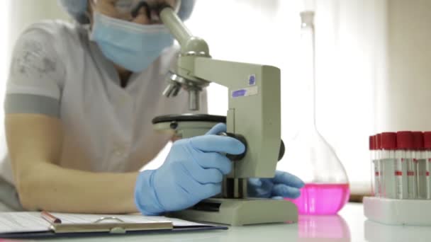 顕微鏡と試験管実験室の条件、女性医学研究者を調査し、メモを取る — ストック動画