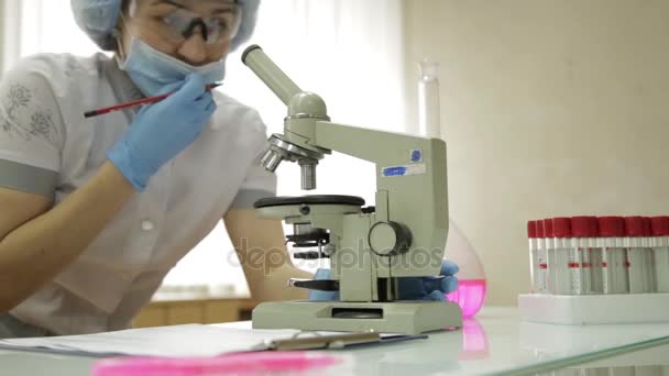 Mujeres investigadoras médicas que trabajan con microscopios y tubos de ensayo en condiciones de laboratorio, investiga y toma notas — Vídeos de Stock