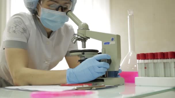 Mikroskoplar ve laboratuvar koşullarında test tüpleri ile çalışan kadın tıbbi araştırmacılar inceler ve notlar alır — Stok video