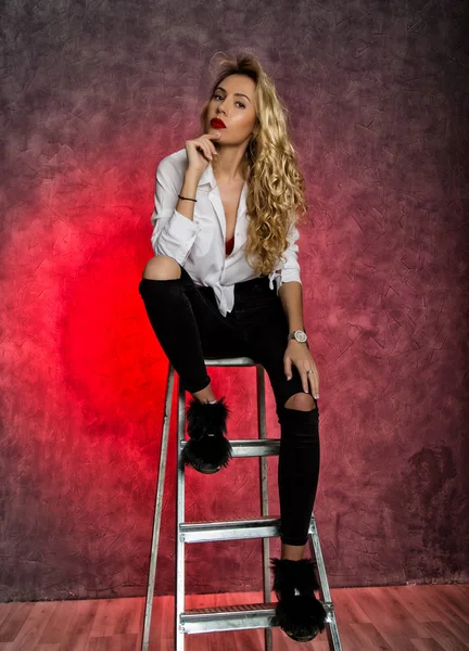 Attractive curly blonde woman sitting on stepladder — Stock Photo, Image
