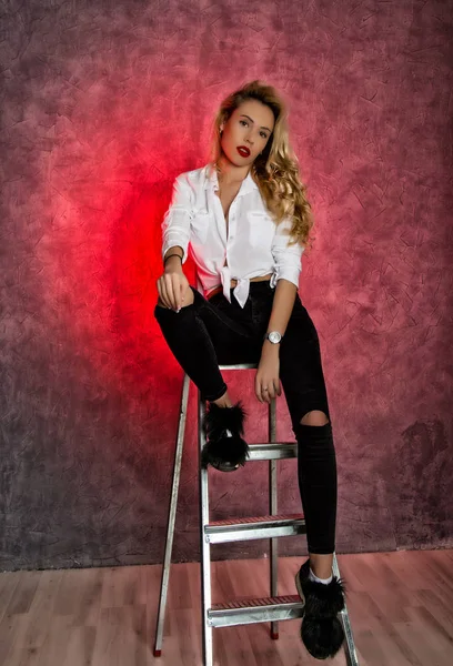 Attraktive lockige blonde Frau sitzt auf Leiter — Stockfoto