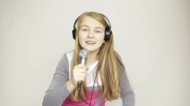 Молода дівчина слухає музику на навушниках, тримає мікрофон, співає і весело танцює — стокове відео