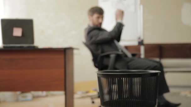 Бездельник в офисе, бизнесмен выбрасывает бумаги в мусорное ведро, мечтает об отпуске — стоковое видео