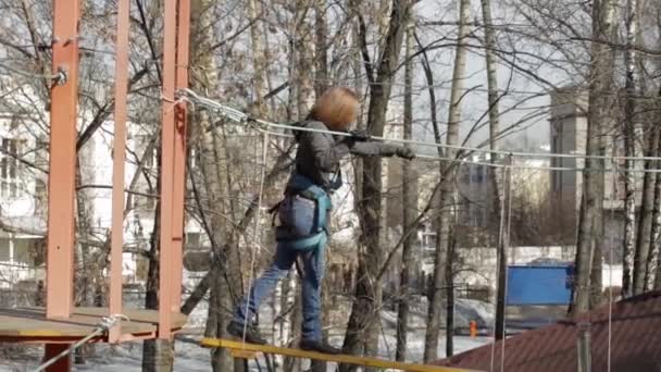 Jonge vrouwelijke klimmer wandelingen door hanger log brug op hoge touwen cursus in extreme park — Stockvideo