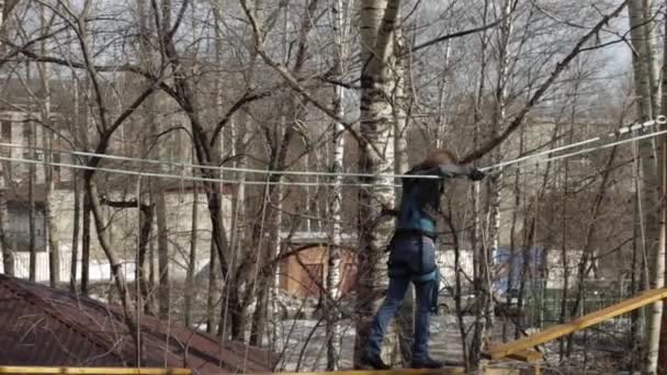 Mladý horolezec žena chodí přívěsek dřevěný most na vysokých lanových překážek v extrémních parku — Stock video