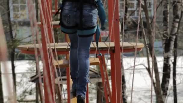 Молодая альпинистка прогуливается по бревенчатому мосту на высоких канатах в экстремальном парке — стоковое видео