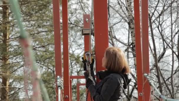 Mladý horolezec žena chodí přívěsek dřevěný most na vysokých lanových překážek v extrémním parku. unfastens karabina — Stock video