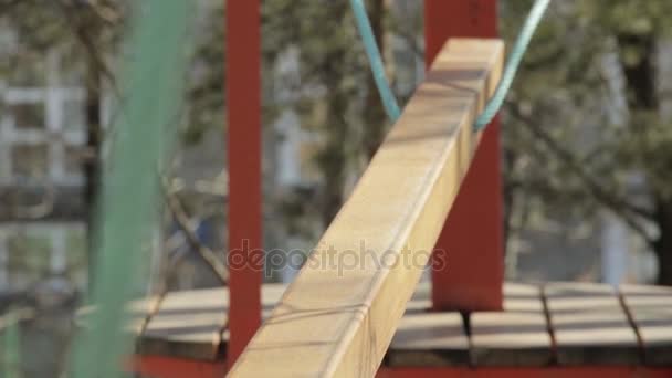 Young female climber walks by pendant log bridge on high ropes course in extreme park — Stock Video