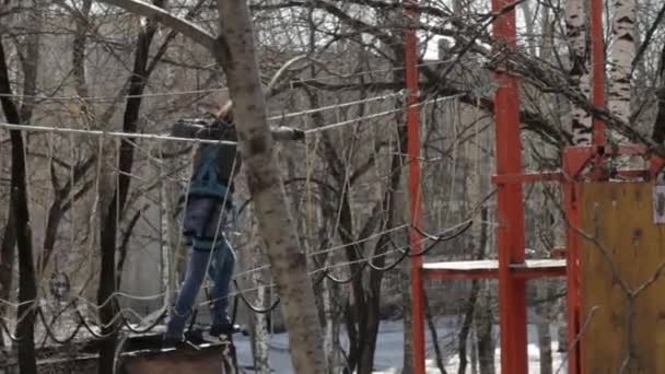 Jovem alpinista caminha pela ponte de corda pingente no curso de cordas altas no parque extremo. Conceito de escalada — Vídeo de Stock