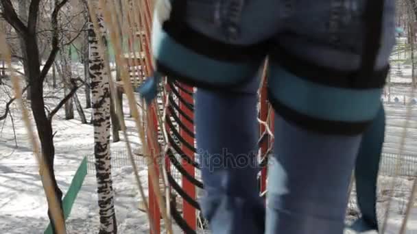 Joven escaladora camina por puente de cuerda colgante en el curso de cuerdas altas en el parque extremo. Concepto de escalada — Vídeo de stock